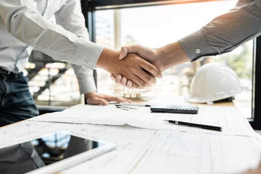 Builder and client shaking hands over table with construction plans