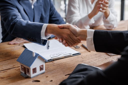 client shaking hands with broker over table with agreement and model of home