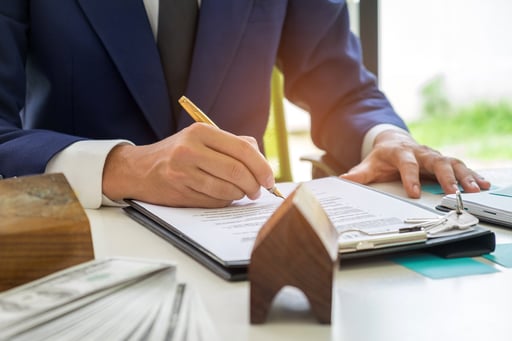 Businessman signing a house contract with money on table