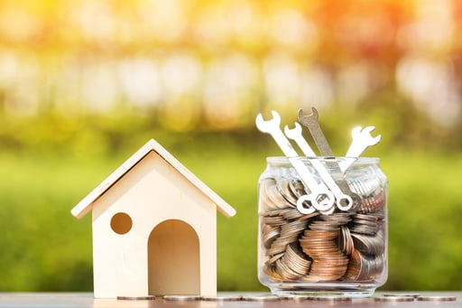 Wooden house model next to jar full of money and repair wrenches