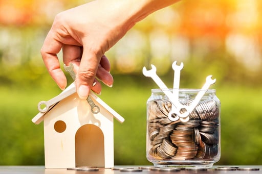 hand repairing house model next to jar full of money