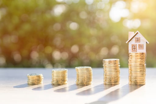 Coin stacks on table growing with house model on top of largest stack