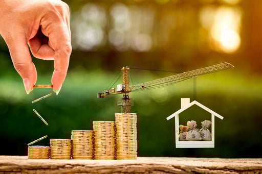 Hand putting coins on stacks with a crane holding up a house filled with money