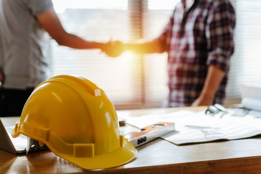 yellow safety helmet on desk with construction team shaking hands