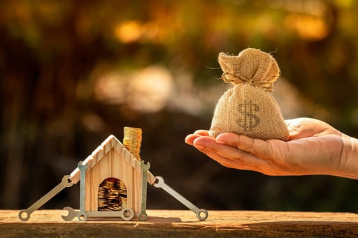 Man hand holding money bag next to wooden house model and construction tools