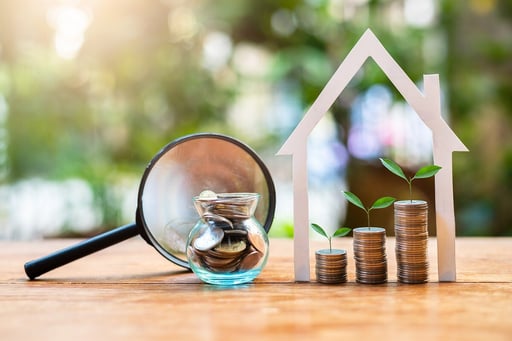 Money coin stacks with house structure and magnifying glass