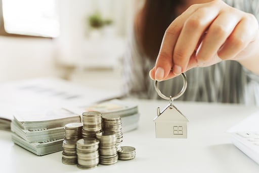 money and coin stacks next to hand holding house keychain