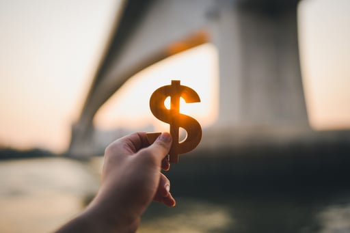 Hand holding dollar symbol with blurred bridge in background