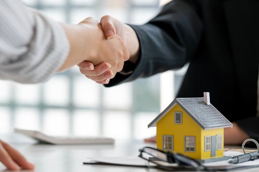 Handshake over table with signed agreement and model of home