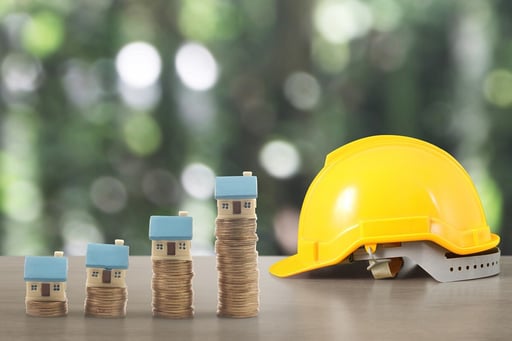 Yellow hardhat and model houses on growing coin stacks