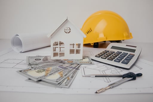 Construction drawings with helmet, calculator, money, and model of house
