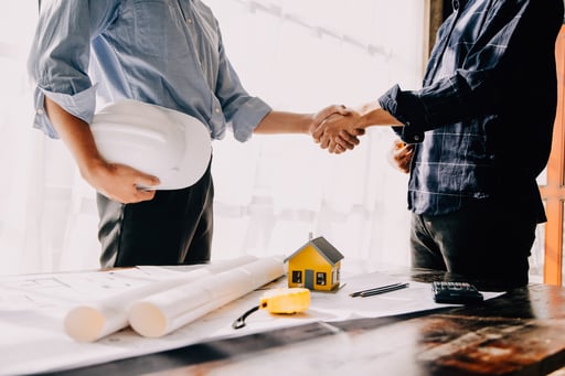 Builder and architect shake hands over table with blueprint, tools, and model of home