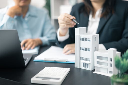 Real estate brokers sitting at table with model of multifamily property, laptop, and calculator