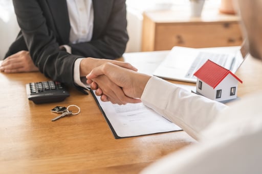 Real estate deal client shaking hands with broker over agreement and model of home