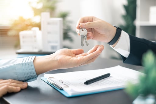 Broker handing over key to home with agreement and apartment model on table