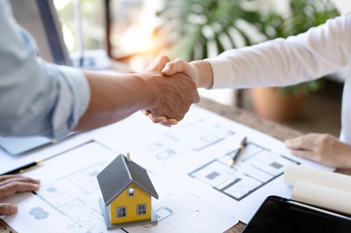 engineer shaking hands with client over table with blueprints and model of home