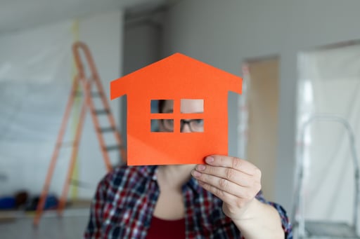 person proudly holding an orange houseshaped cutout in their hand in a home undergoing renovation
