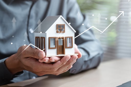 Mortgage broker holding model house in his hands with line graph increasing