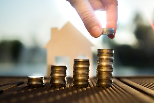 hand putting coins on growing stacks with house model in background